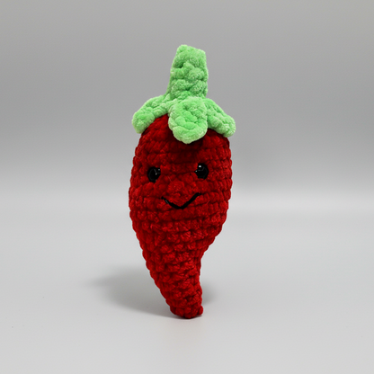 Crocheted red chili pepper toy with green leaves on a white background