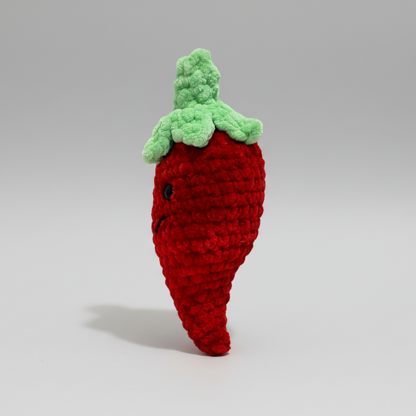 Crocheted red chili pepper toy with green leaves on a white background
