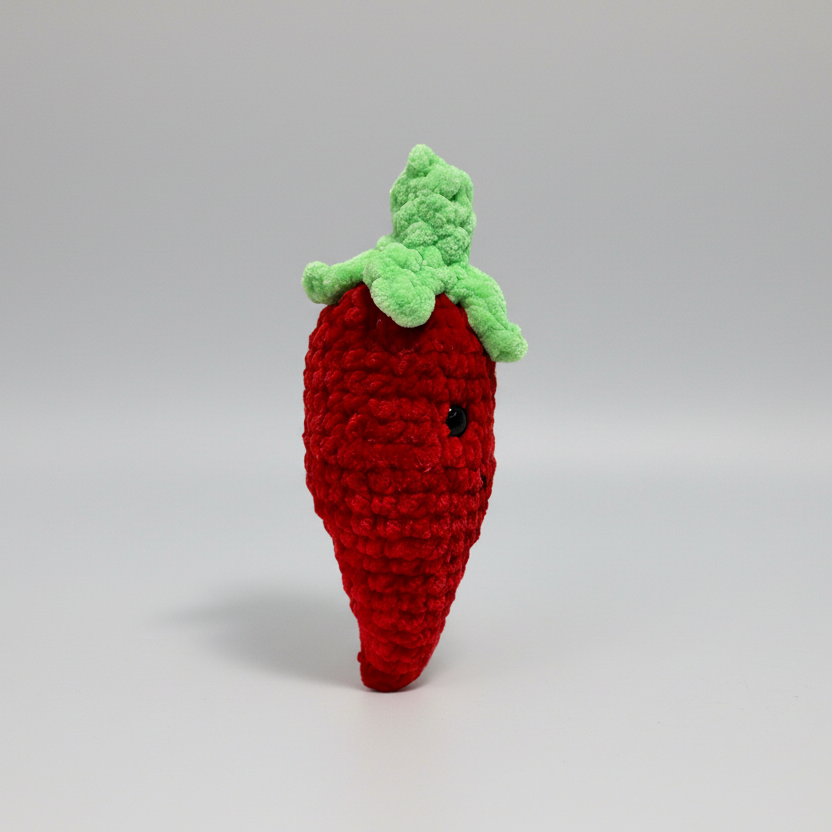 Crocheted red carrot toy with green leaves on a white background