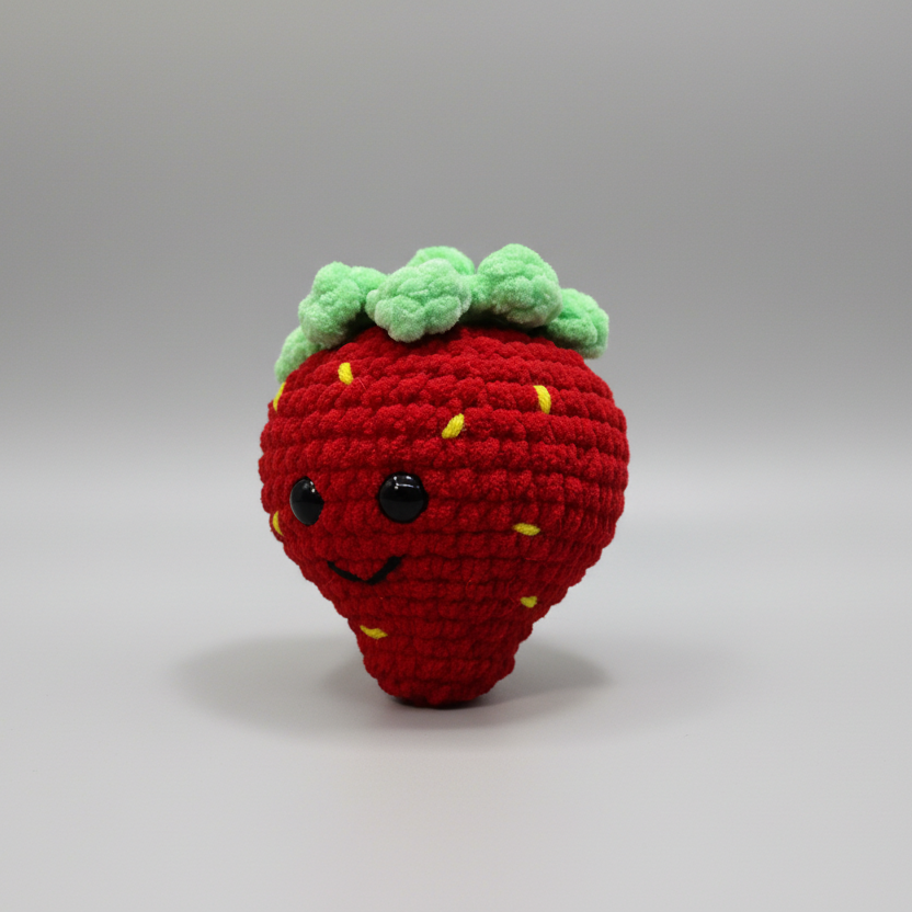 Crocheted strawberry toy with green leaves on a white background