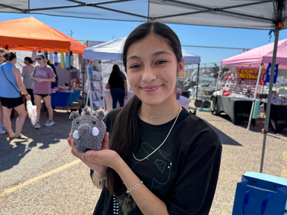Woman holding a small crochet javelina at an farmers market